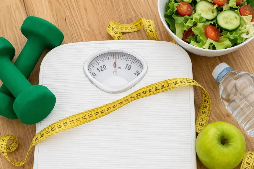 Balança, fita métrica, halteres e salada, representando o tratamento da obesidade e o emagrecimento